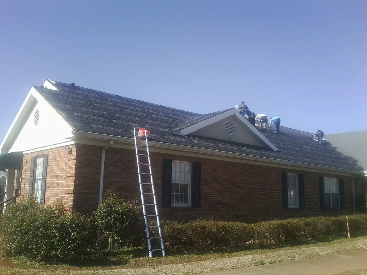 Crew tearing shingles off a brick ranch roof with a ladder set — Emergency Roof Repair work by our crew in Sidney