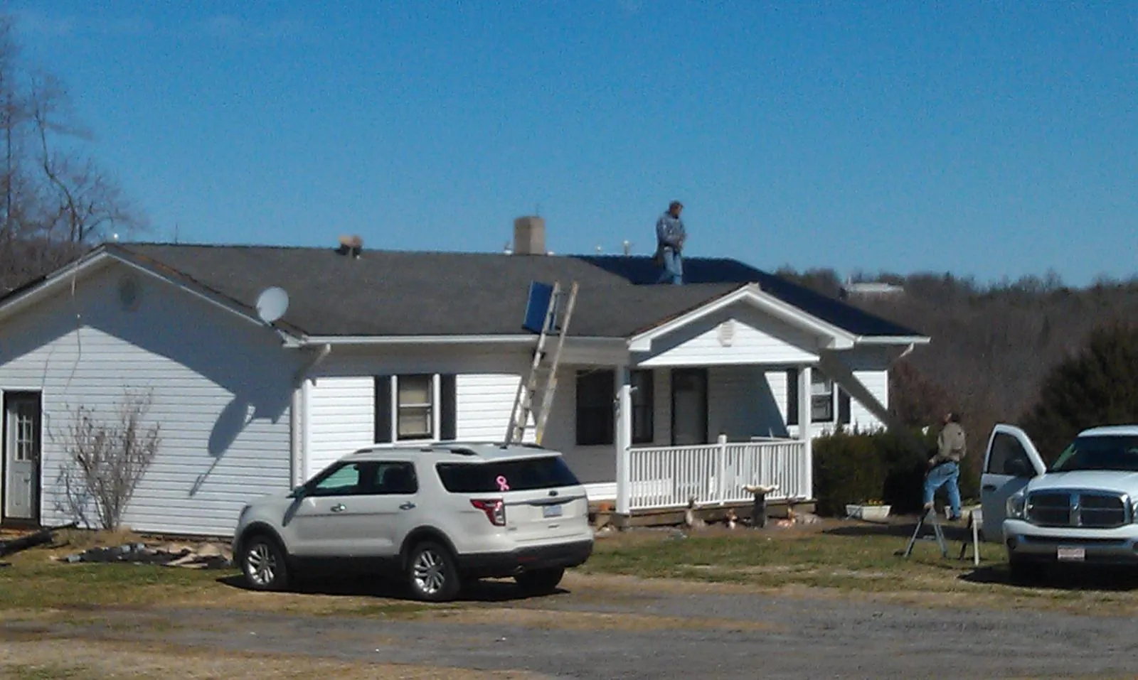Roofers stripping shingles from a white ranch house roof in Sidney
