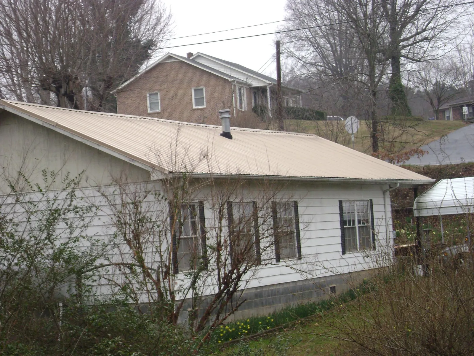 Tan metal roof on a white sided house set into a hillside — Commercial Roofing by Roofing Brothers in Sidney